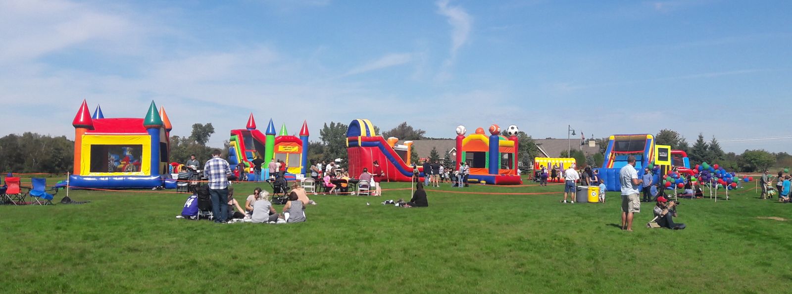 Giant inflatable slide, bounce house, combo, and other inflatables at a church field event.